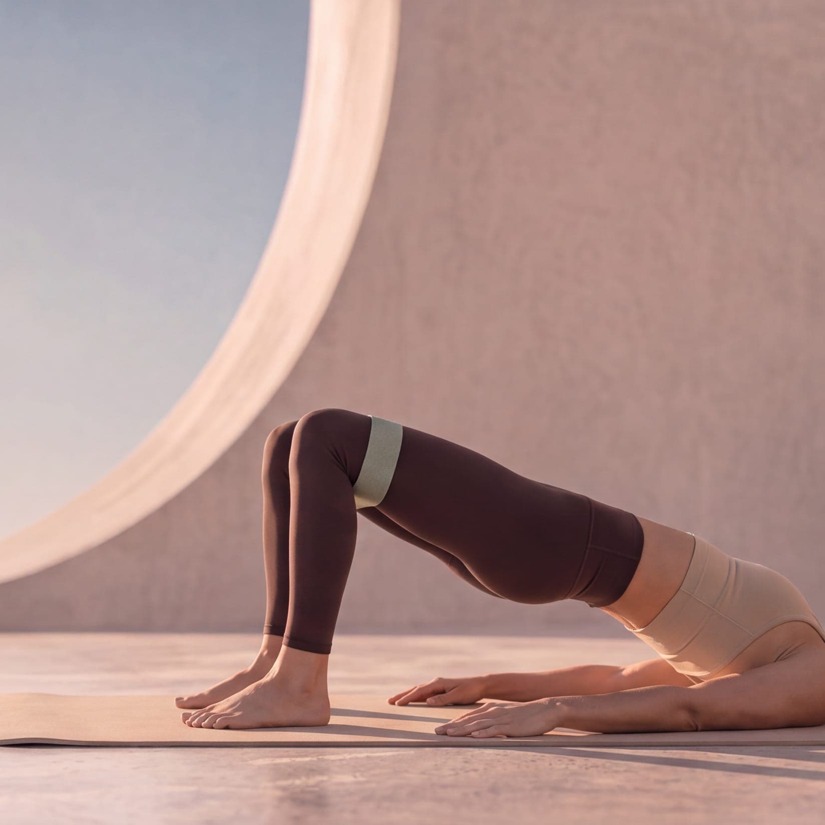 A woman in a glute bridge with a mini band above her knees, on a mat against the sky