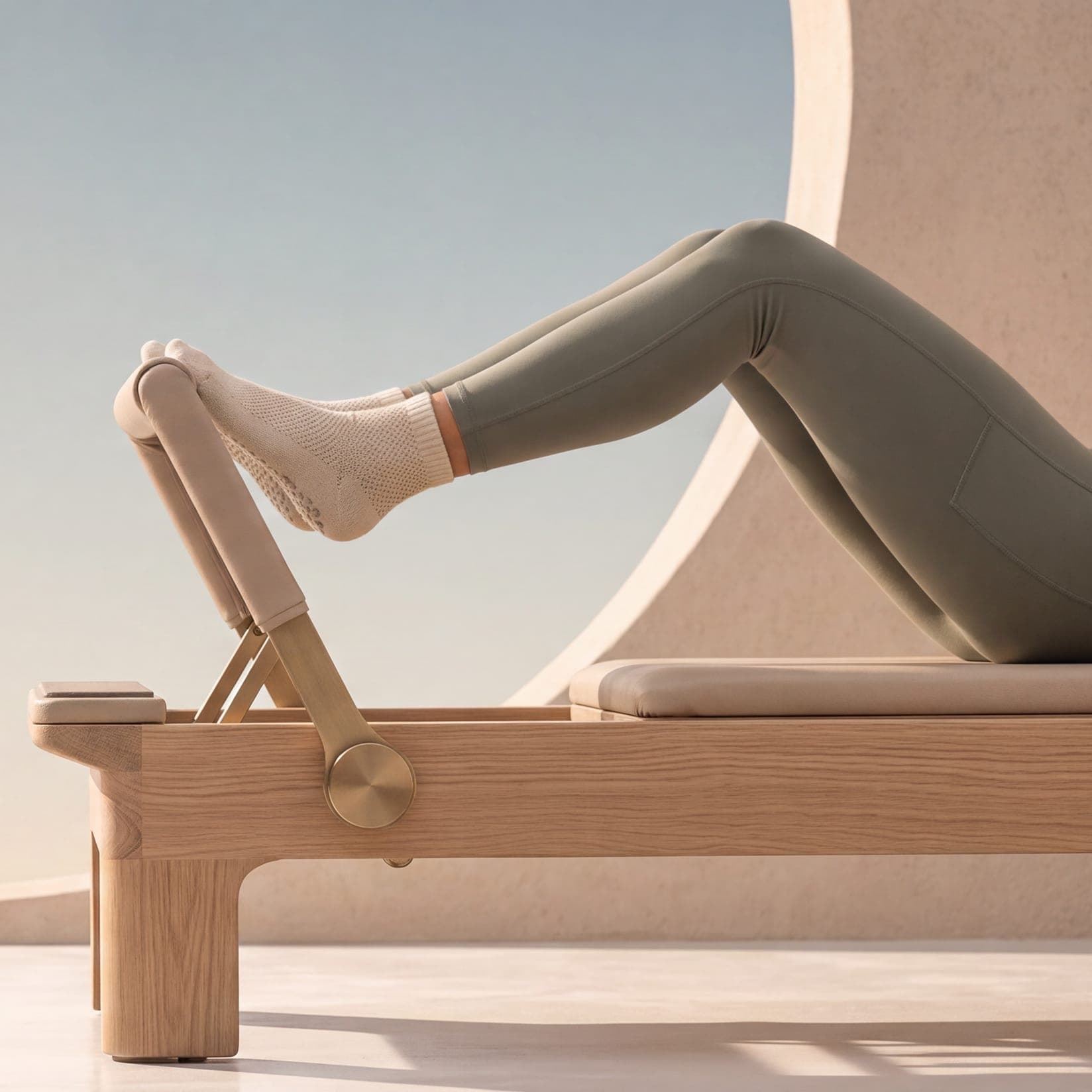 Füße in Socken drücken gegen die Fußstange eines Reformers aus hellem Holz