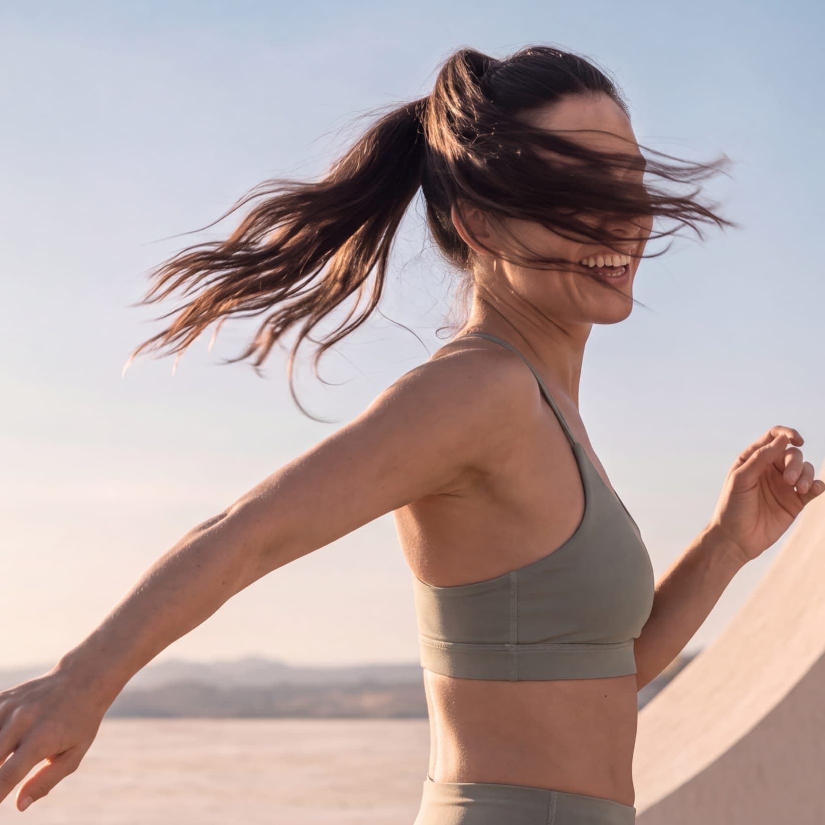 A woman laughing mid-turn, her ponytail flying against the sky