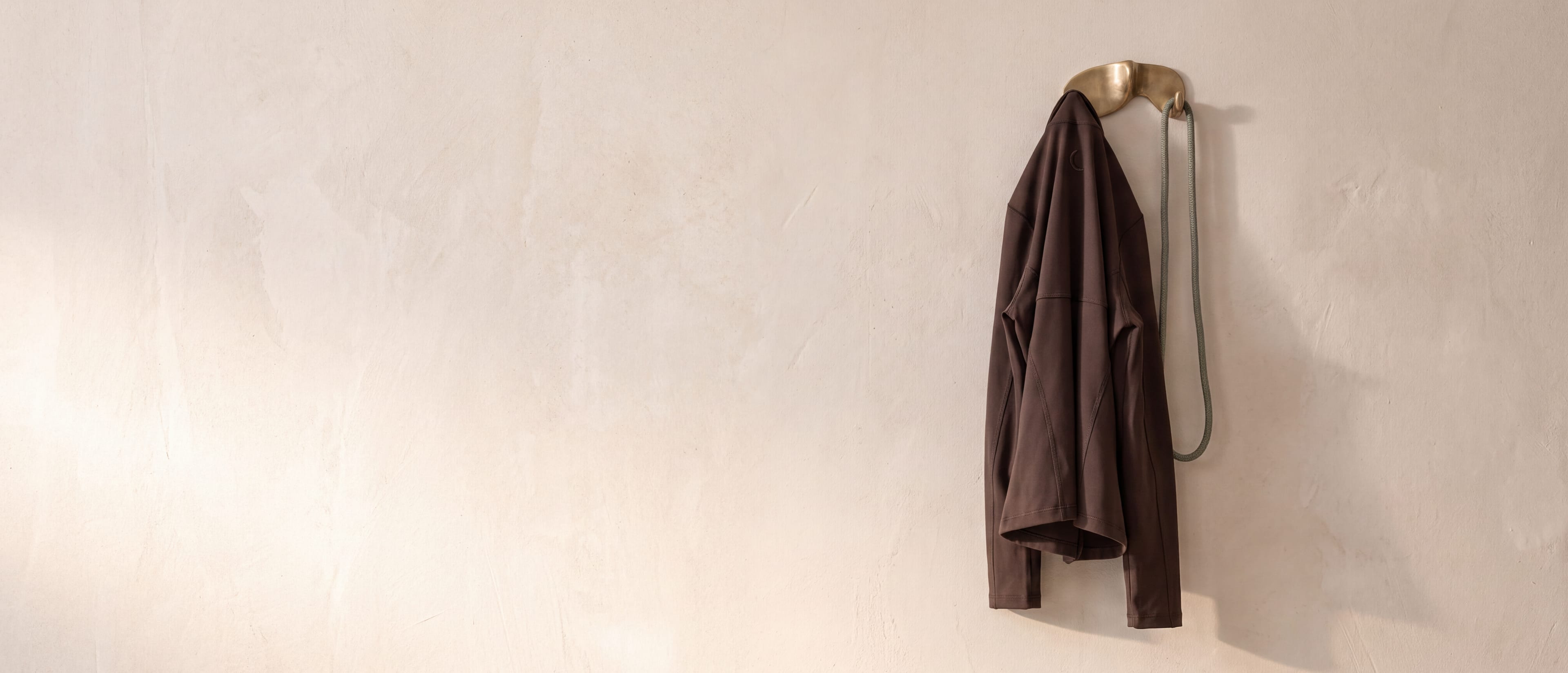 Eine Trainingsjacke in Espresso mit gesticktem Mond hängt an einem Messinghaken