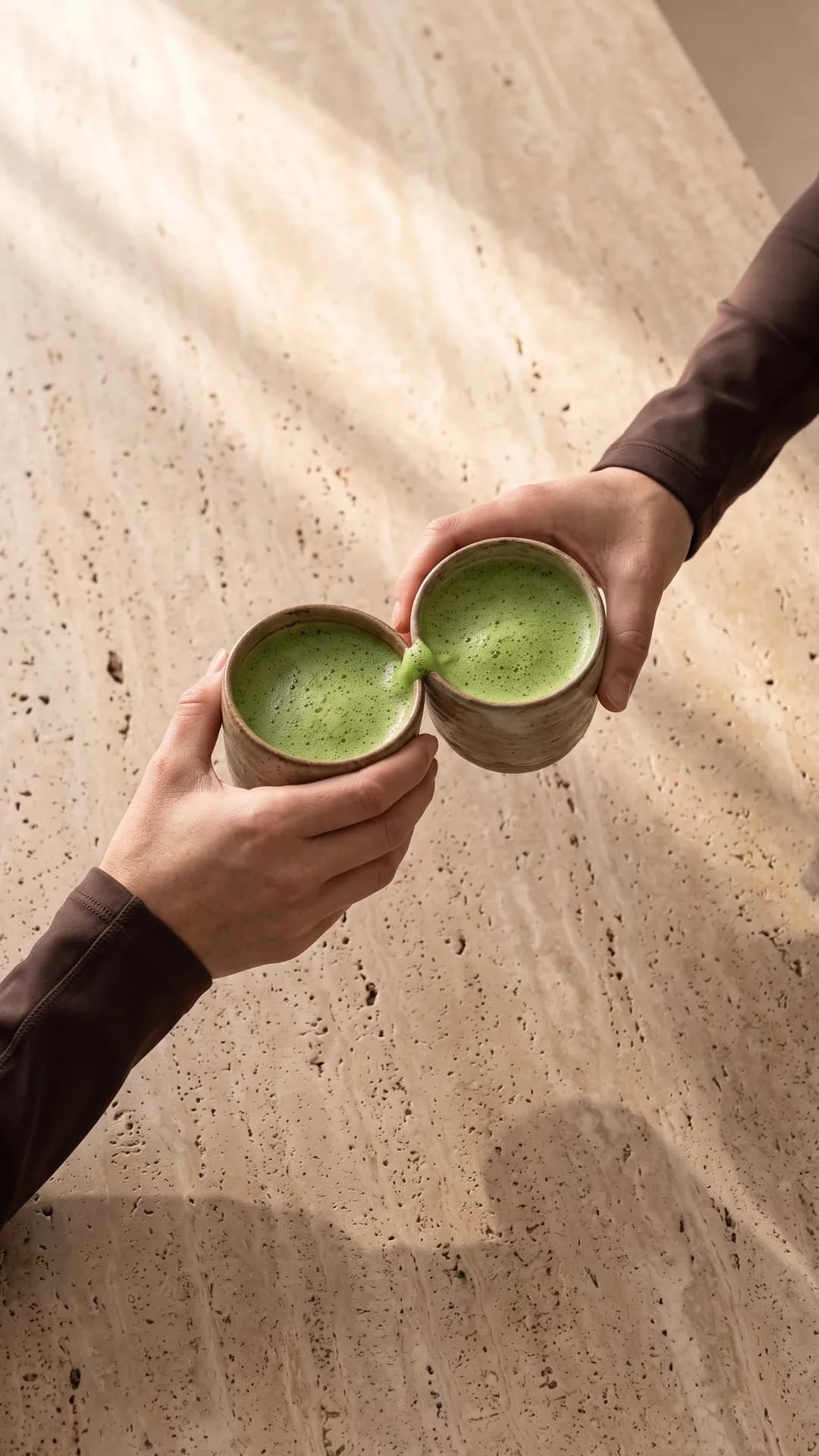 Zwei Hände stoßen vor der Öffnung mit Matcha an
