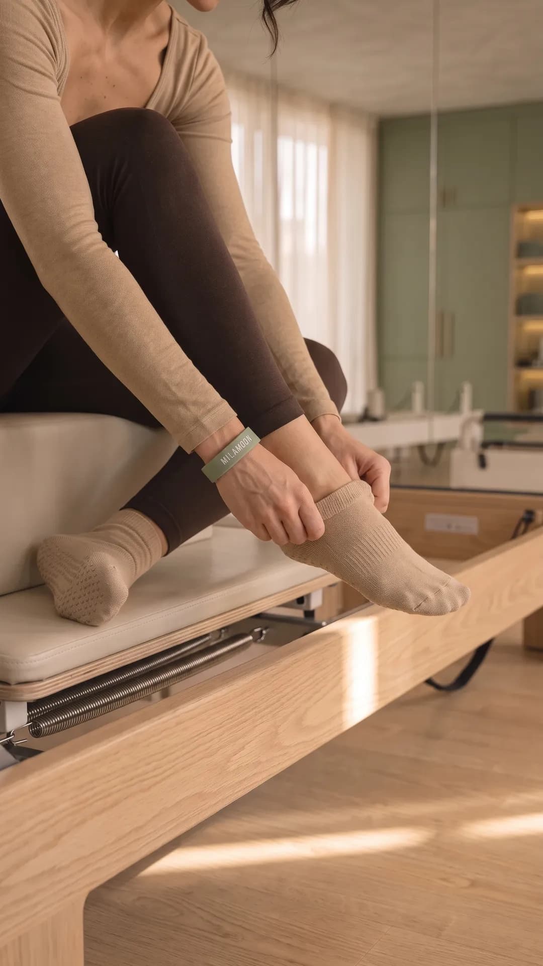 Eine Frau zieht auf der Kante eines Reformers Rutschsocken an, am Handgelenk das MILA-MOON-Armband